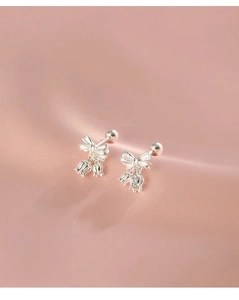 Close-up of silver bow stud earrings with lily of the valley drops on pink silk