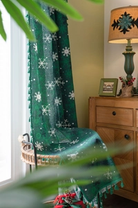 Detail of dark green Christmas curtain with white snowflakes and decorative tassels