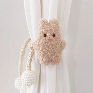 Detail of plush bear curtain tieback with woven rope and shiny pearl accents
