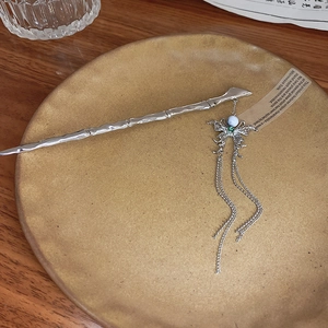 Detail of silver butterfly hairpin with bamboo-style wand and flowing tassels on ceramic tray