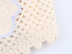 Macro view of cream crochet fabric with hollow knit textures and light blue embroidered lines