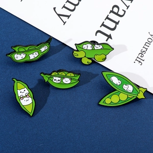 Detail of creative green pea pod cat enamel pins set on a dark blue textured background