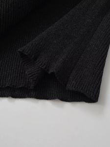 Macro detail of black wool poncho showing high-quality chunky knit texture and clean hemline