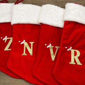 Detailed top view of four red velvet Christmas stockings with gold glitter embroidered letters