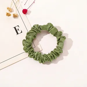 Detail of army green satin scrunchie with silky pleated fabric texture and elegant sheen