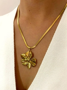 Detail of a gold snake chain necklace featuring a bold 3D floral pendant on a model