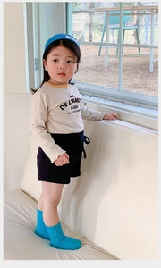 Detail of cream long sleeve shirt and navy shorts on child model in bright room