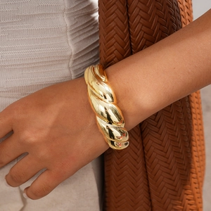 Detail of chunky gold-plated twisted cable bracelet on a woman wearing a knit sweater