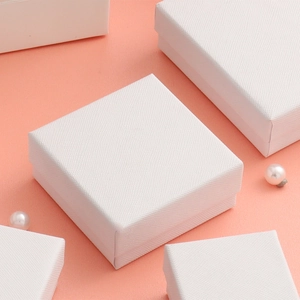 Detailed view of white square jewelry gift boxes with elegant fabric texture and pearls