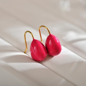 Macro shot of vibrant pink teardrop earrings with elegant gold hooks on a textured surface