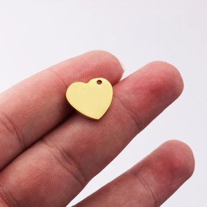 Polished gold heart charm pendant held by fingers, showing smooth stainless steel surface