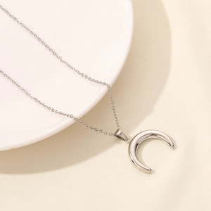 Polished silver moon pendant on a delicate chain resting on a white ceramic plate