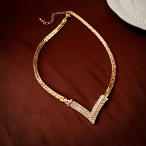 Detail view of a vintage V-shaped gold plated necklace with crystals on a textured fabric