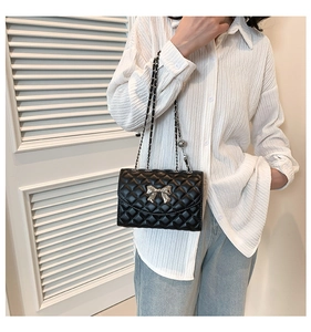 Close-up of black quilted shoulder bag with silver bow buckle and chain strap on model