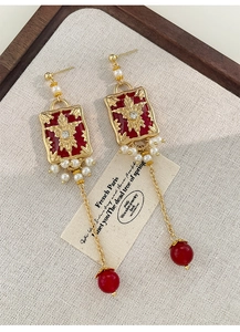 Detail of red enamel earrings with gold floral relief, pearls and long tassels