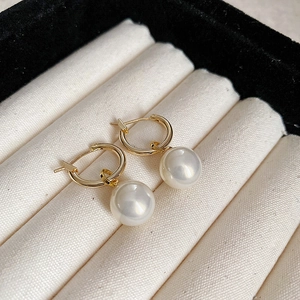 Eleganti orecchini a cerchio dorati con perle bianche su un cuscino per gioielli