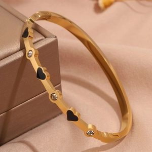 Vista macro di bracciale dorato con cuori neri e inserti di diamanti bianchi brillanti