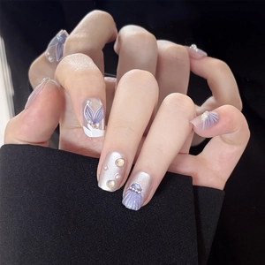 Close-up of lilac mermaid style press-on nails with shell carving and pearl details