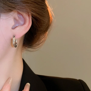 Close-up of a silver oval hoop earring with polished finish on a model's ear