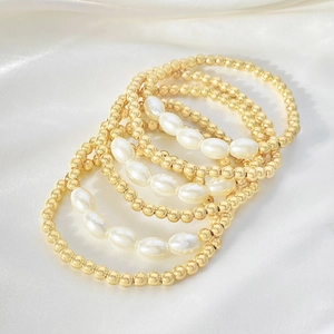 Dettaglio del set di braccialetti con perline dorate e perle bianche su seta bianca