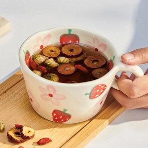 Detailed view of hand-painted strawberry ceramic mug on wooden tray with herbal tea