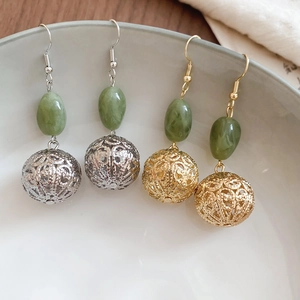 Détail de boucles d'oreilles boules évidées en résine or et argent sur céramique