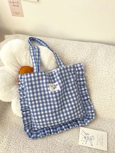 Close-up of blue plaid tote bag with ruffle trim and fun fun party label on plush surface