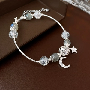Detail of silver beaded bracelet featuring moon and star charms on leather texture