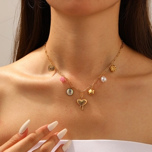 Golden paperclip chain necklace with heart, pearl, and floral charms on a model