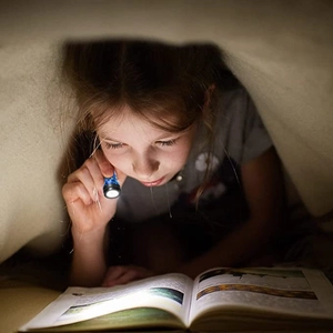 Mini LED finger flashlight used for reading books under a blanket in a cozy night scene
