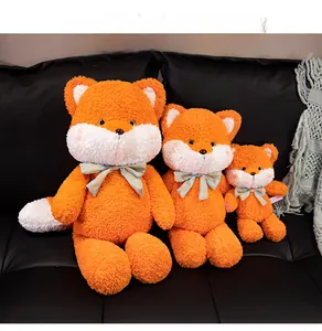 Three sizes of orange plush fox toys with blue checkered bows on a gray sofa