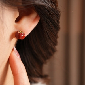 Close-up of vintage red enamel persimmon stud earrings worn on ear with gold metal detail