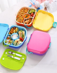 Detail view of colorful bento lunch box with compartments and cutlery on marble surface