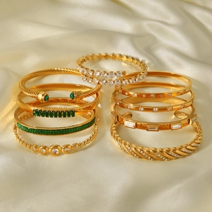 Macro shot of gold bracelets with green gemstones and zircons on white silk background