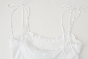 Detail of white spaghetti strap top featuring delicate ruffled neckline and bow tie shoulder