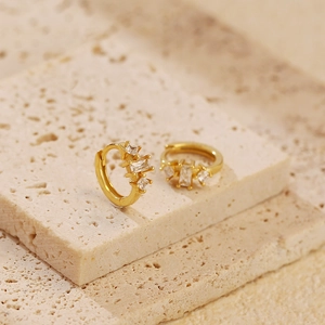 Macro shot of gold hoop earrings with three rectangular zircon stones on textured beige stone