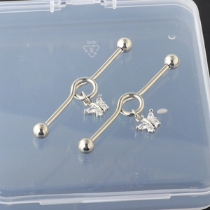 Detail of cross and heart industrial barbell with butterfly zircon charms on clear box