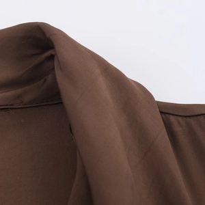 Gros plan sur la texture du tissu marron foncé et les coutures de la robe midi ceinturée