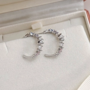 Close-up of C-shaped silver earrings with multicolor zircon stones on a white stand