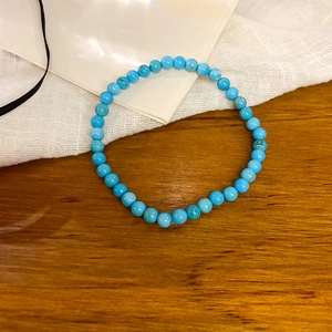 Detailed close-up of sky blue turquoise beaded elastic bracelet on a wooden background