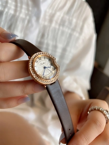 Close-up of rose gold watch with crystal bezel, white dial and brown leather strap