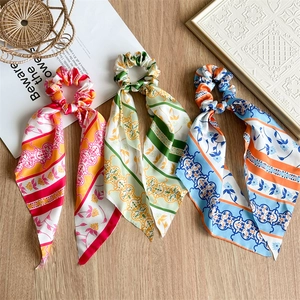 Close-up of three silk bow scrunchies with floral patterns on a wooden background