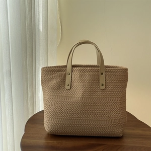 Detail of woven straw tote bag with brown leather handles and rivet accents