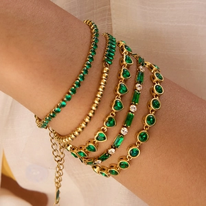 Close-up of gold layered bracelets set featuring green zircon and heart charms on wrist