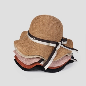 Stack of woven sun hats in five colors featuring wave brims and elegant ribbon bows