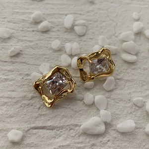 Detail of square zircon earrings with wavy gold borders on a minimalist stone background