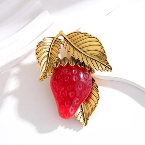 Macro shot of vintage strawberry brooch with red resin texture and golden metal leaves