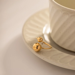 Minimalist gold plated double ball open ring on white ceramic tray background