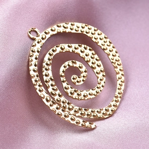 Detailed view of a gold spiral pendant with hammered texture on pink silk fabric