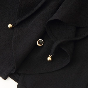 Close-up of black ruffled texture fabric with elegant gold metal button and pendant details